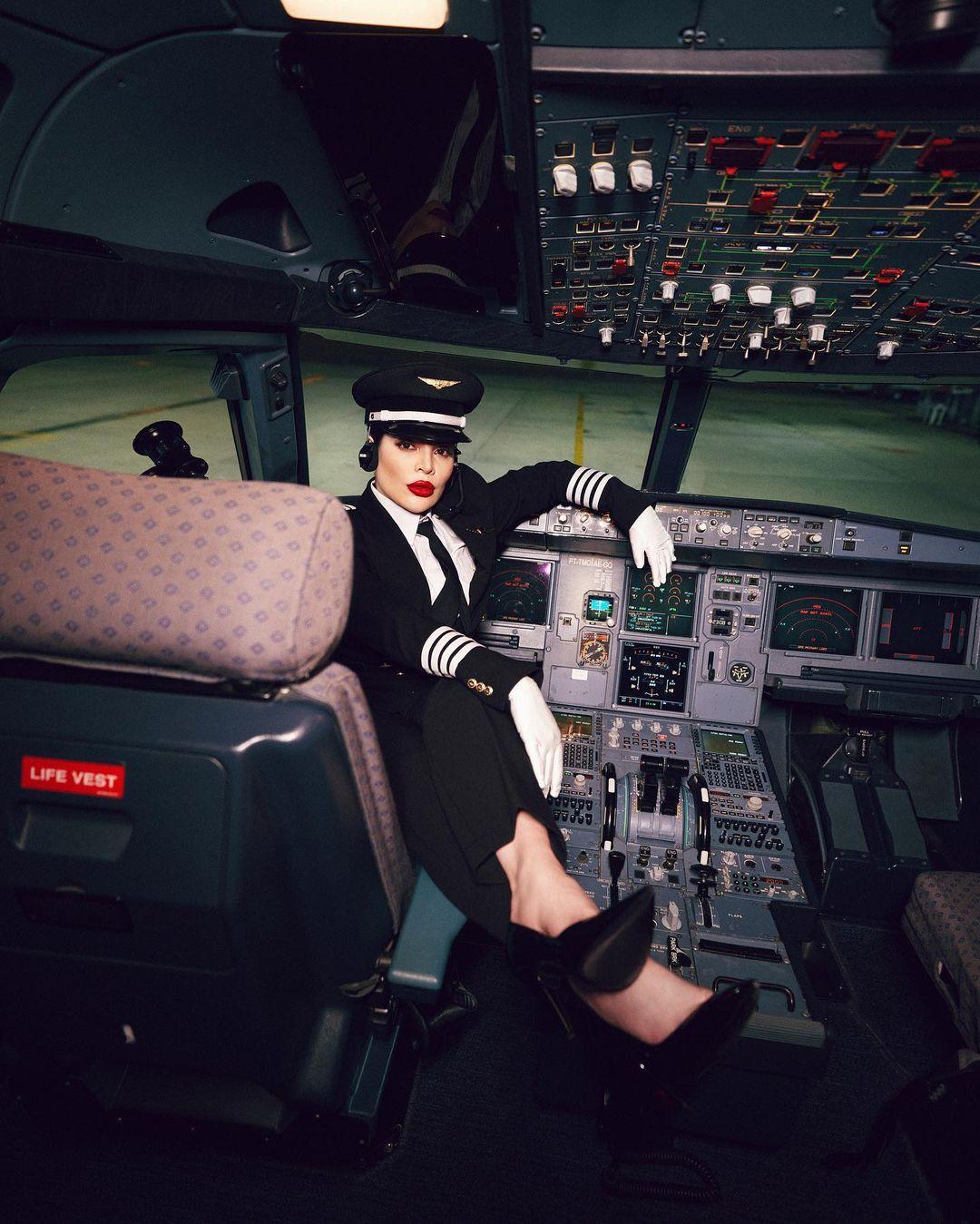 Gkay vestida de piloto posando na cadeira da cabine de um avião