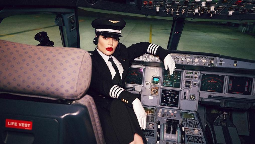Gkay vestida de piloto posando na cadeira da cabine de um avião