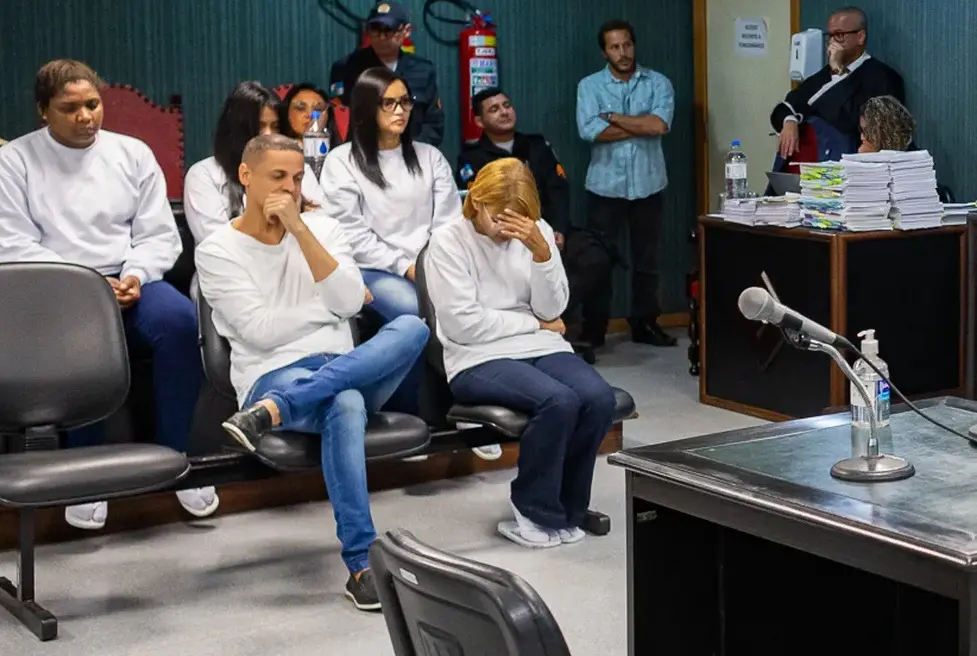 Flordelis sentada no banco de réus de cabeça baixa e com a mão escondendo o rosto. Ela está vestida de branco