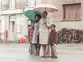 Elenco de Bienvenue À Marly- Gomont em pé na chuva durante cena do filme