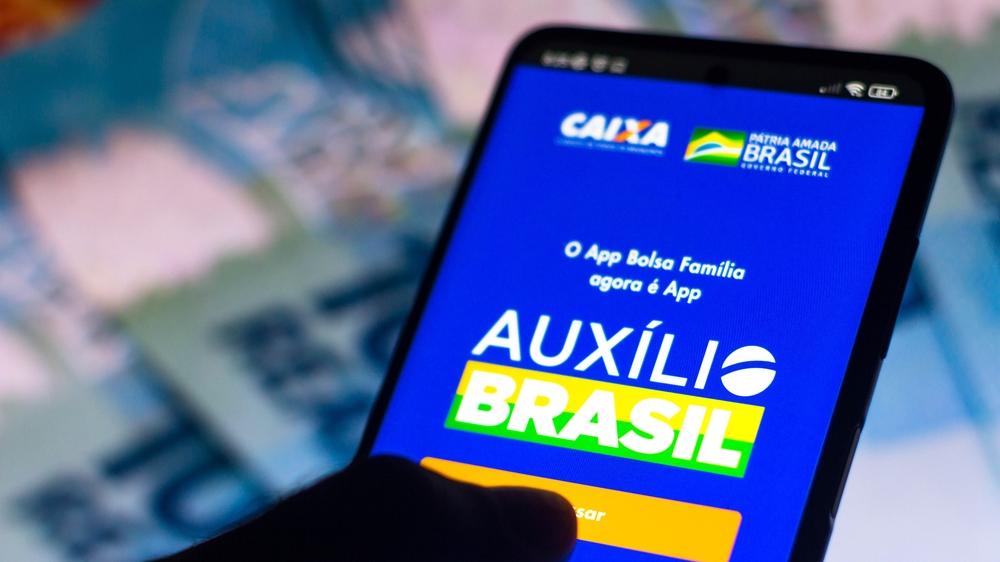 Mão segura celular aberto no aplicativo do Auxílio Brasil, da Caixa