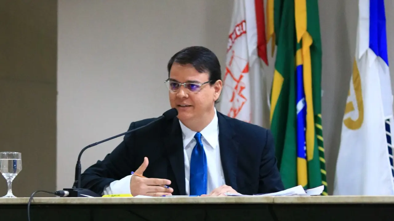 José Hercy é um homem branco de meia idade e de cabelos pretos e lisos. Ele usa um terno preto, camisa de botão branca e gravata azul. Também usa óculos