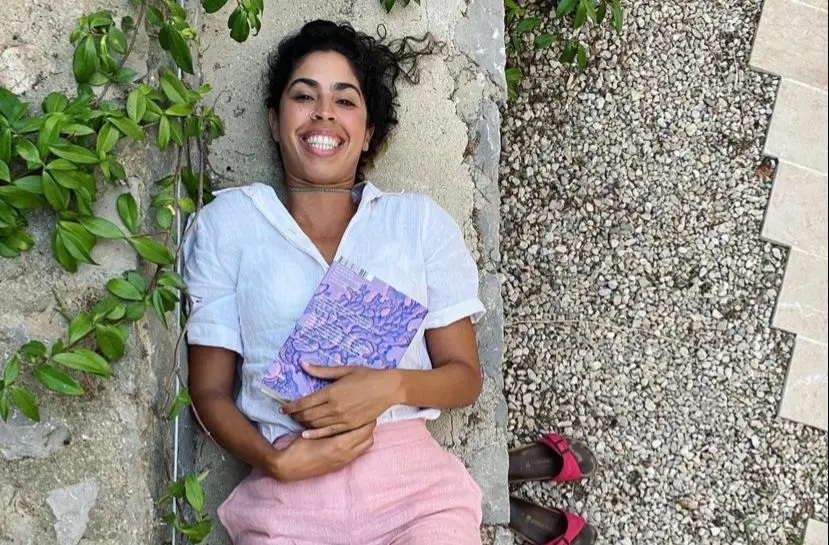 Bela Gil está deitada com um livro da capa lilás sobre a barriga