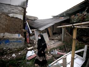Mulher caminha por entre destroços de casas na Indonésia