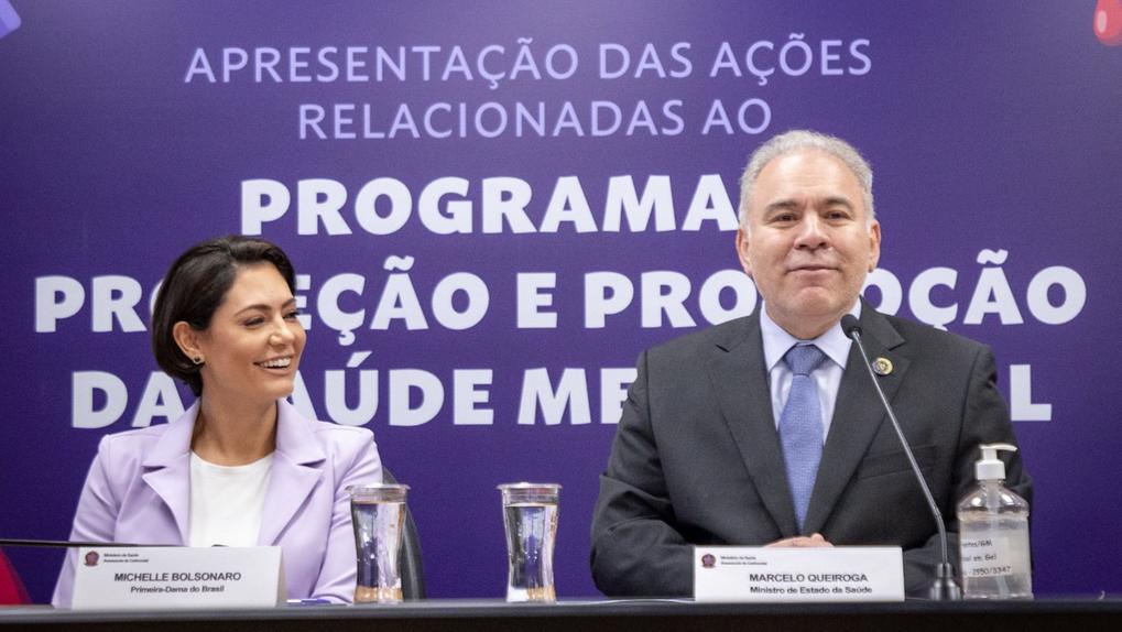 Michele Bolsonaro está de perfil. Ela sorri enquanto olha para o ministro Marcelo Queiroga.