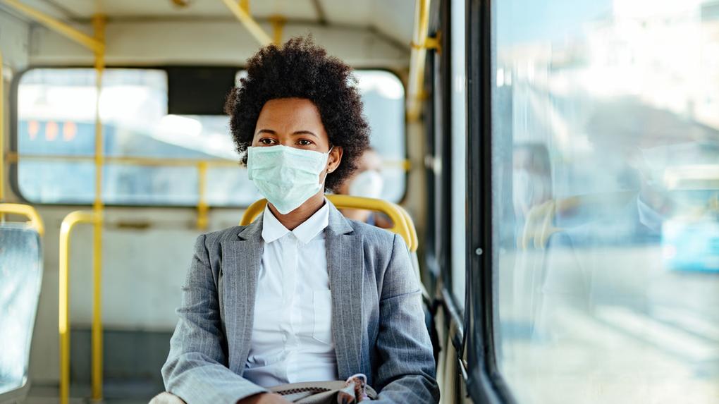 Imagem mostra mulher negra usando máscara de proteção a bordo de um ônibus público