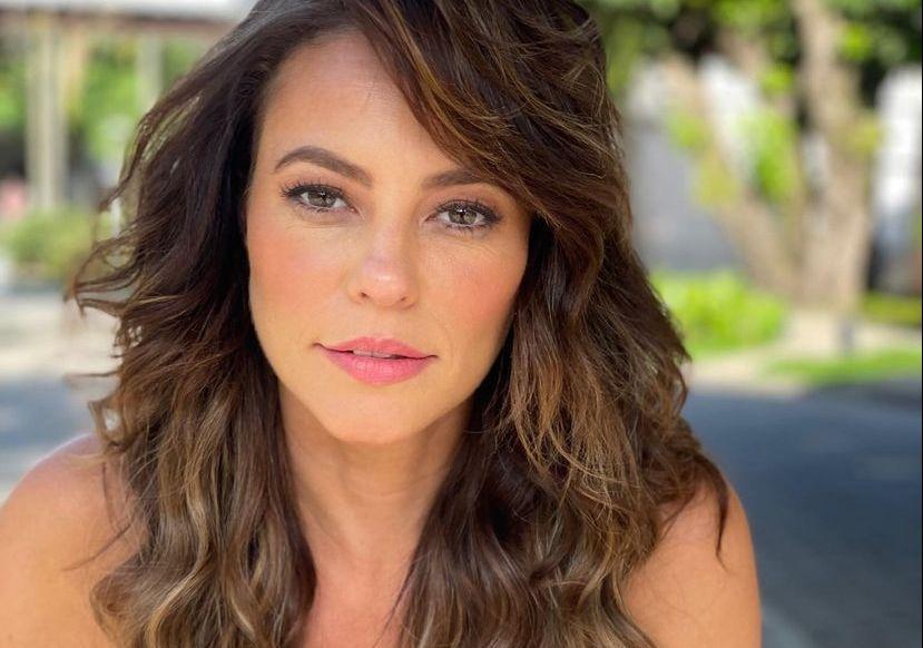 Paolla Oliveira é uma mulher branca e de cabelos ondulados castanho escuros. Ela está séria e usa batom rosa