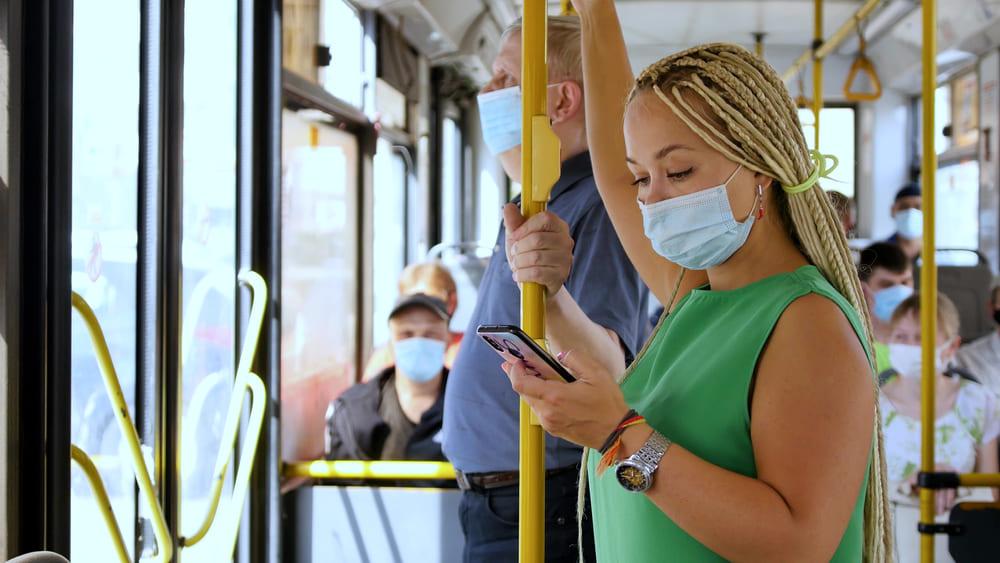 Mulher de máscara observa o celular enquanto utiliza o transporte público