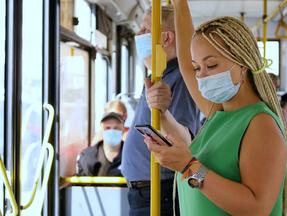 Mulher de máscara observa o celular enquanto utiliza o transporte público