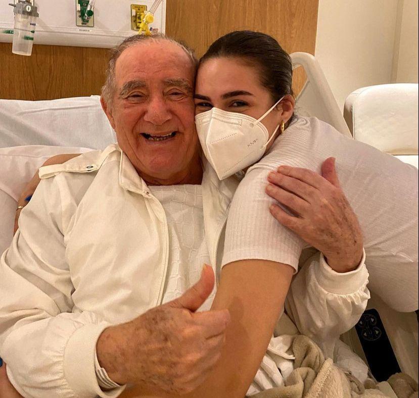 Renato Aragão sorri ao abraçar a filha, Lílian, que está de máscara