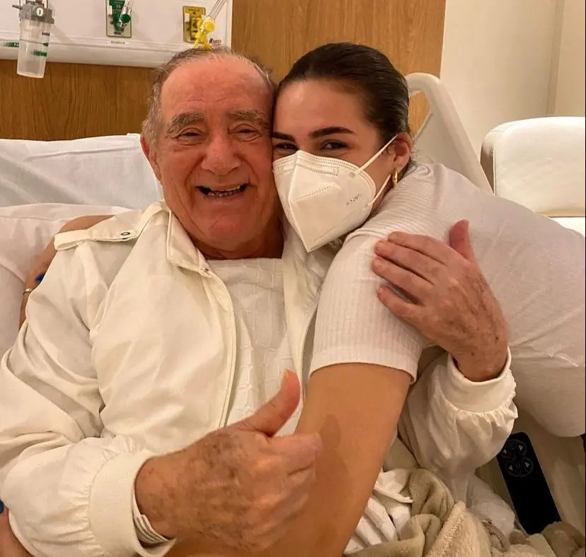 Renato Aragão sorri ao abraçar a filha, Lílian, que está de máscara