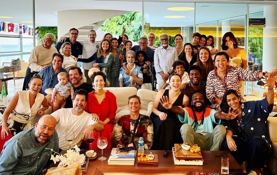 foto de vários atores sentados em sofá, em pé e no chão