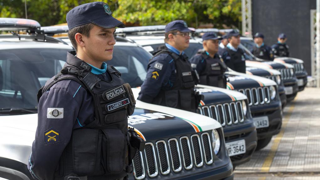 Agentes da Polícia Militar do Ceará dispostos em fila ao lado de viaturas