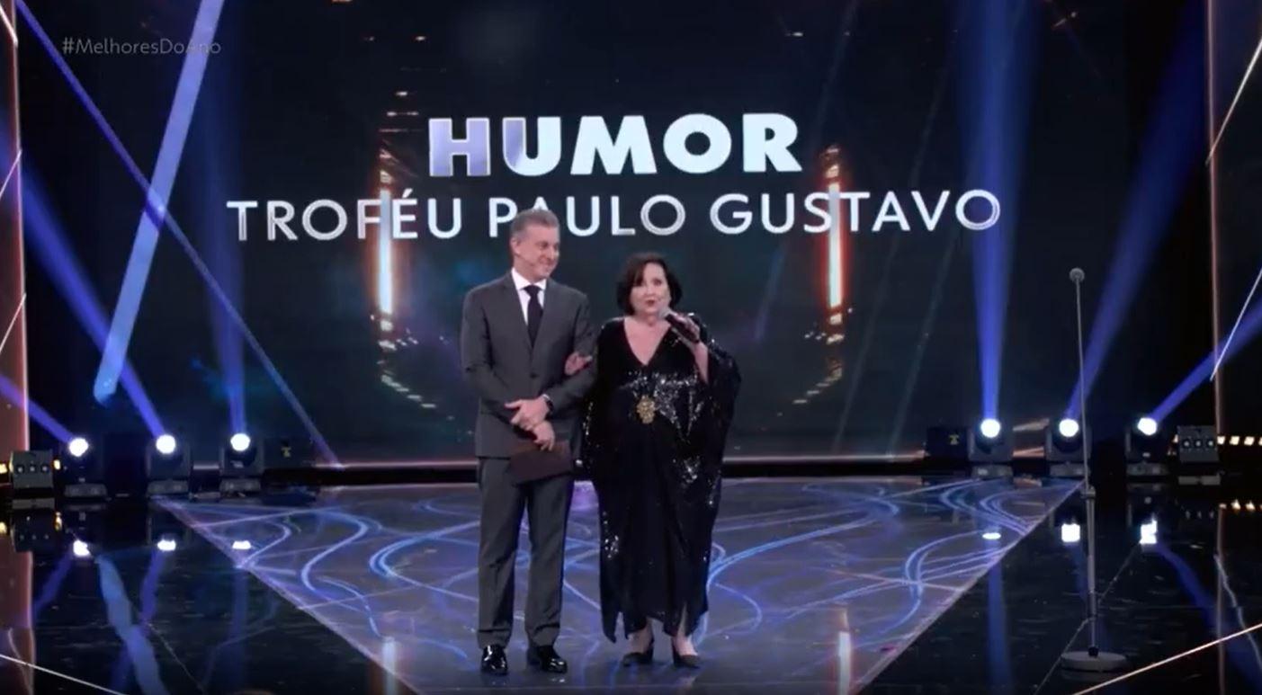 luciano huck e dea lucia diante de telão com as palavras humor troféu paulo gustavo