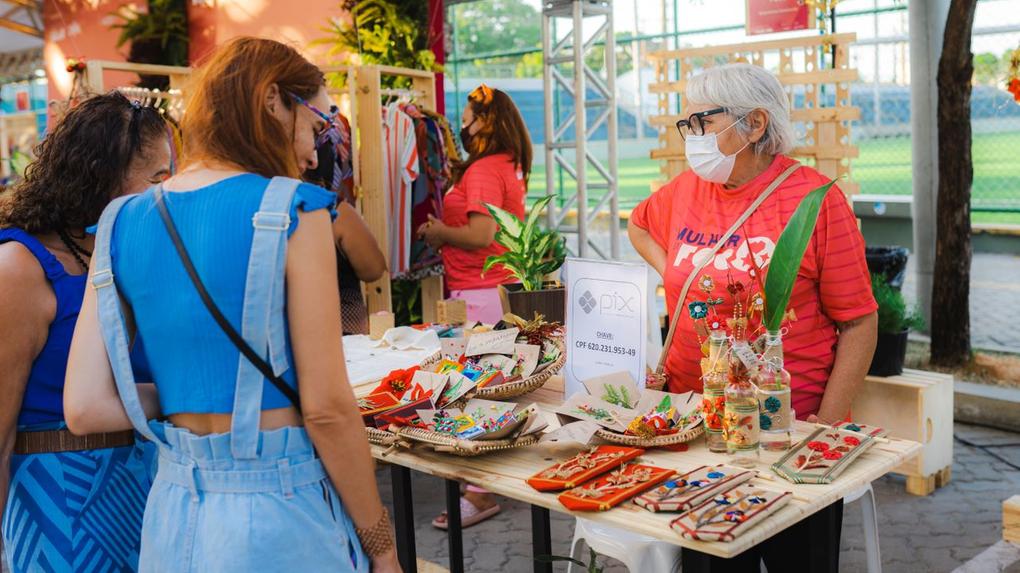 mulher expoe itens em feira de artesanato e estande é visitado por mulheres