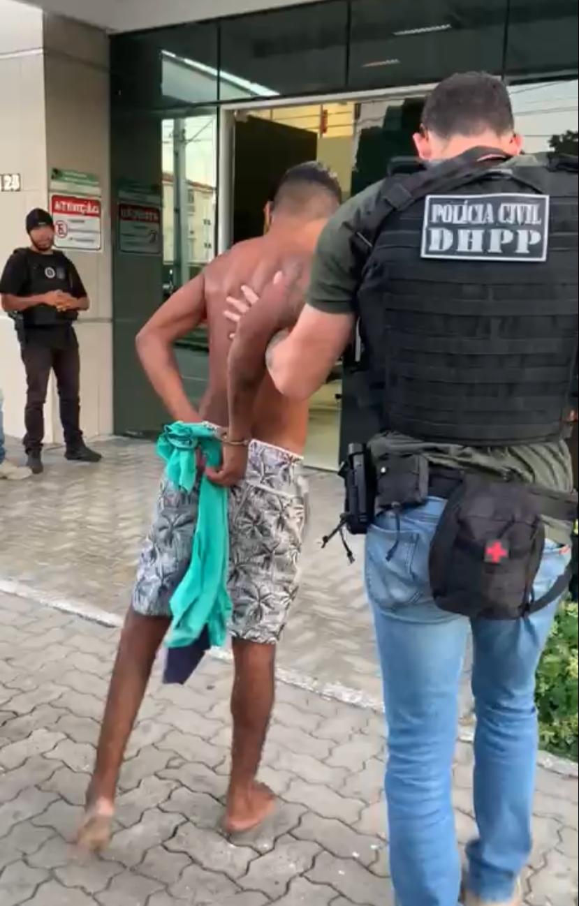 Homem sem camisa e de bermuda é levado por um policial civil para a delegacia