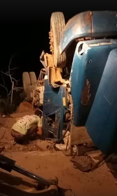 Homem de blusa branca abaixado ao lado de caminhão azul tombado em Mauriti, no Ceará