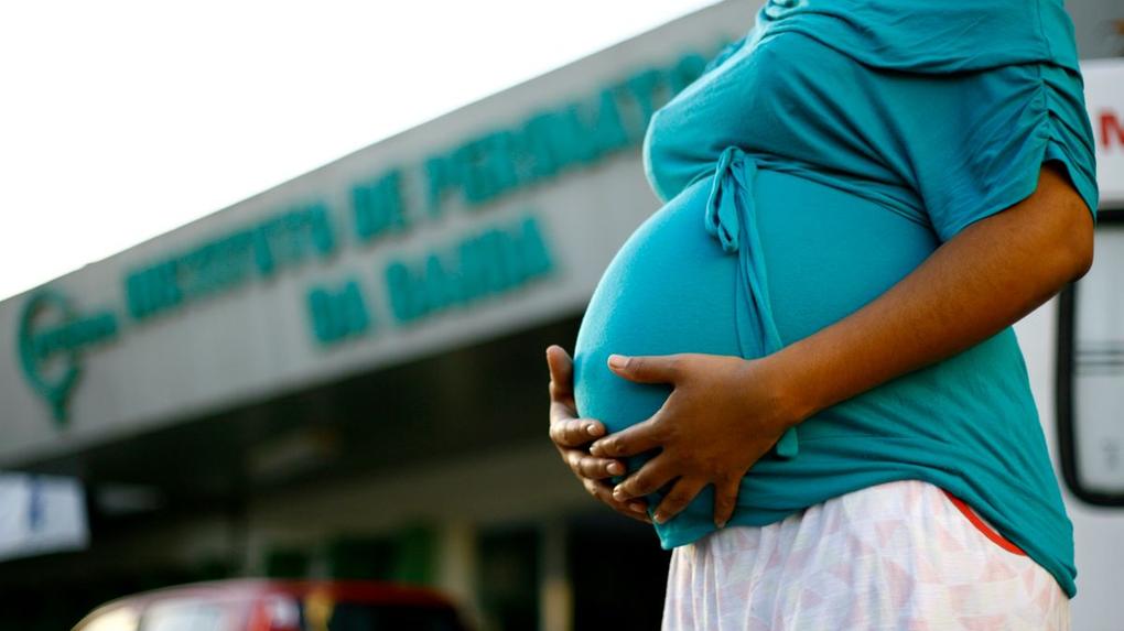 Mulher grávida segurando barriga em frente a hospital