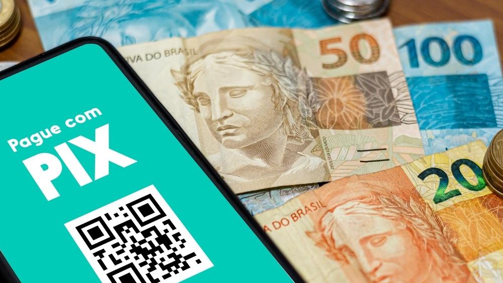 Celular com a legenda pague com pix em cima de cédulas de 20, 50 e 100 reais