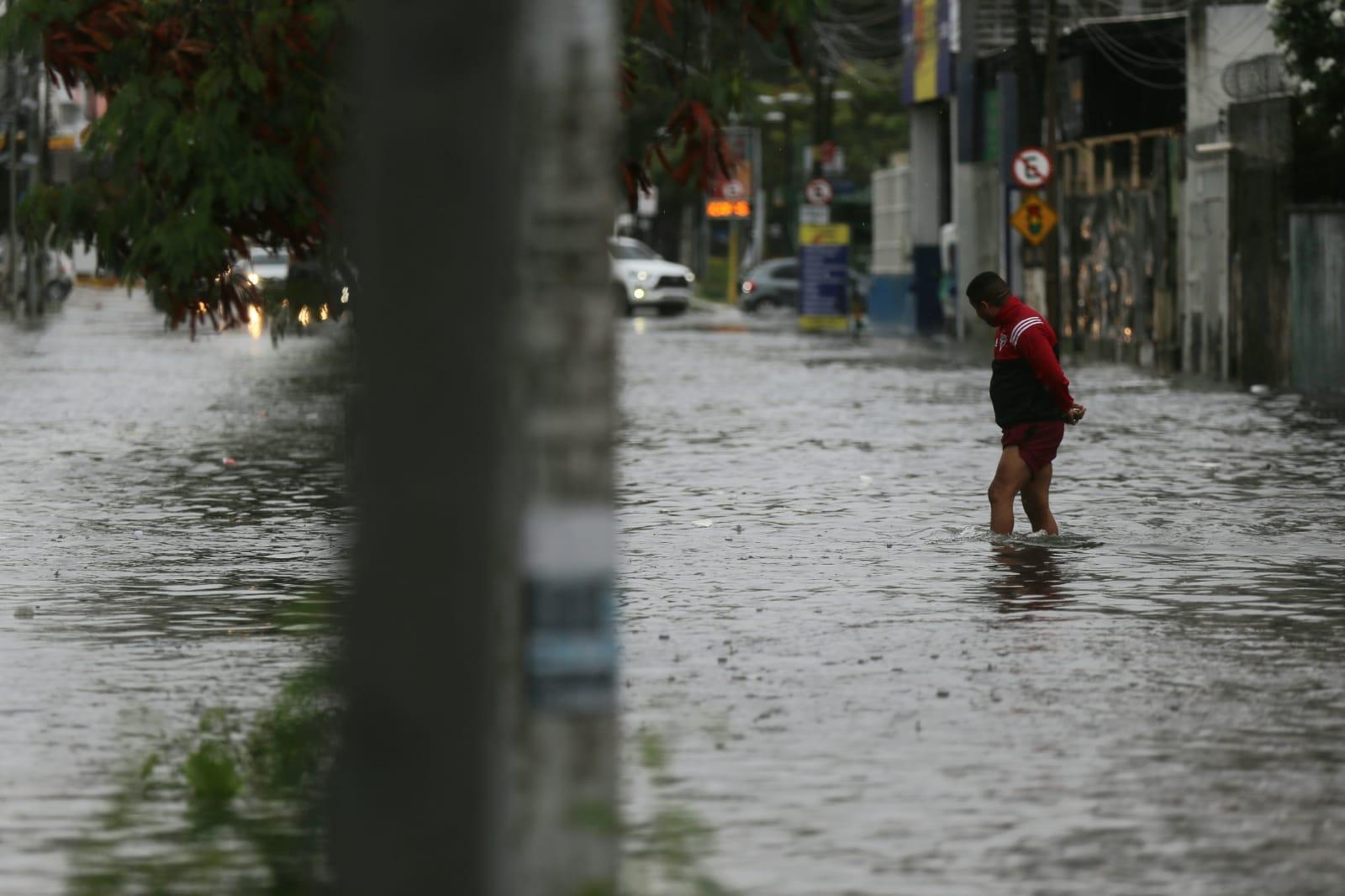 Pedestre atravessa rua alagada em Fortaleza
