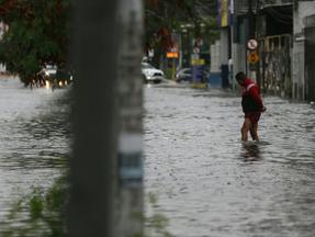 Pedestre atravessa rua alagada em Fortaleza