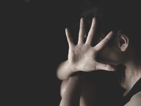 Foto com fundo preto mostra mulher com a cabeça escondida e a mão estendida para o lado, para pedir para parar