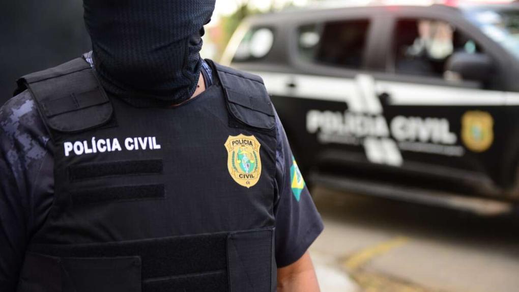 Agente da Polícia Civil do Ceará usando colete à prova de balas, próximo à viatura