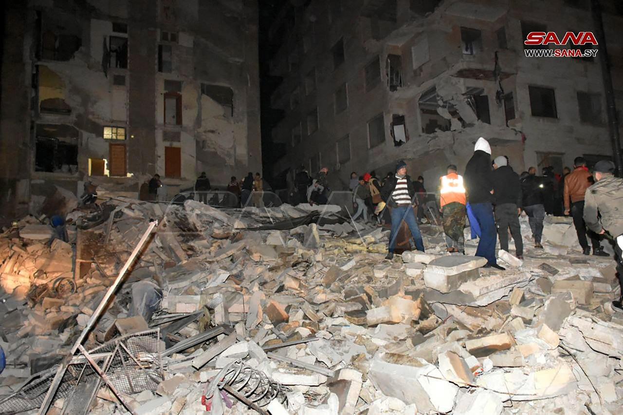 Nesta foto de folheto tirada pela agência de notícias Sana em Hama, Síria, em 6 de fevereiro de 2023, equipes de resgate procuram vítimas de um prédio de oito andares que desabou após um terremoto de magnitude 7,8 no sul da Turquia.