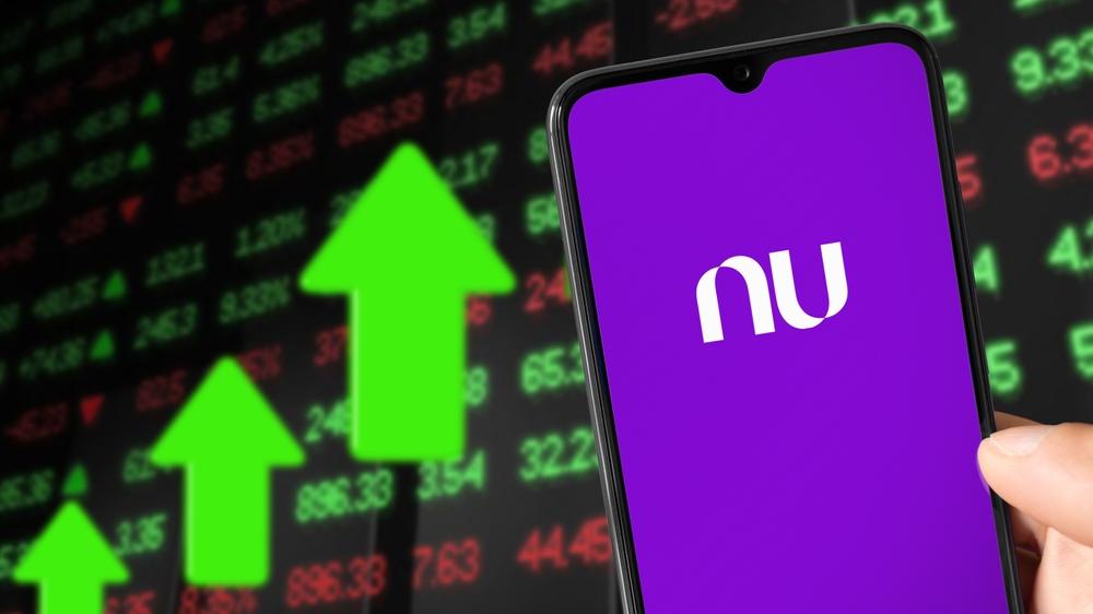 Imagem mostra um celular no aplicativo Nubank e símbolos de investimentos ao fundo