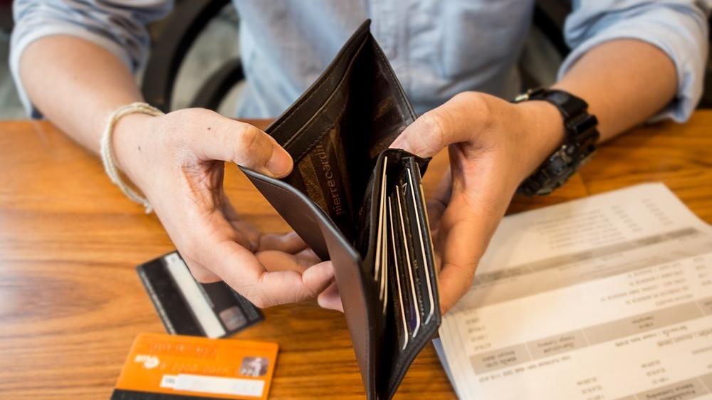 Mão abre carteira vazia em cima de mesa com cartões de crédito