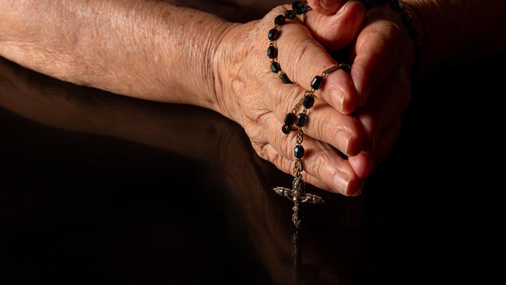 Mãos juntas em oração com terço religioso