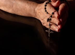 Mãos juntas em oração com terço religioso
