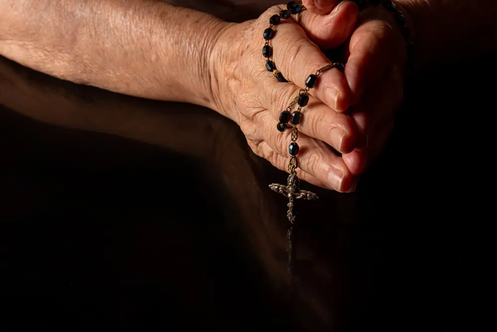Mãos juntas em oração com terço religioso