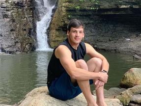 Rickson Brito sentado em pedra de cachoeira