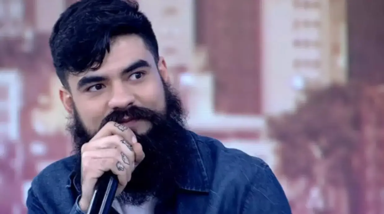 Pedro Gabriel tem barba espessa e cabelo liso, pretos. Ele está com camisa azul.