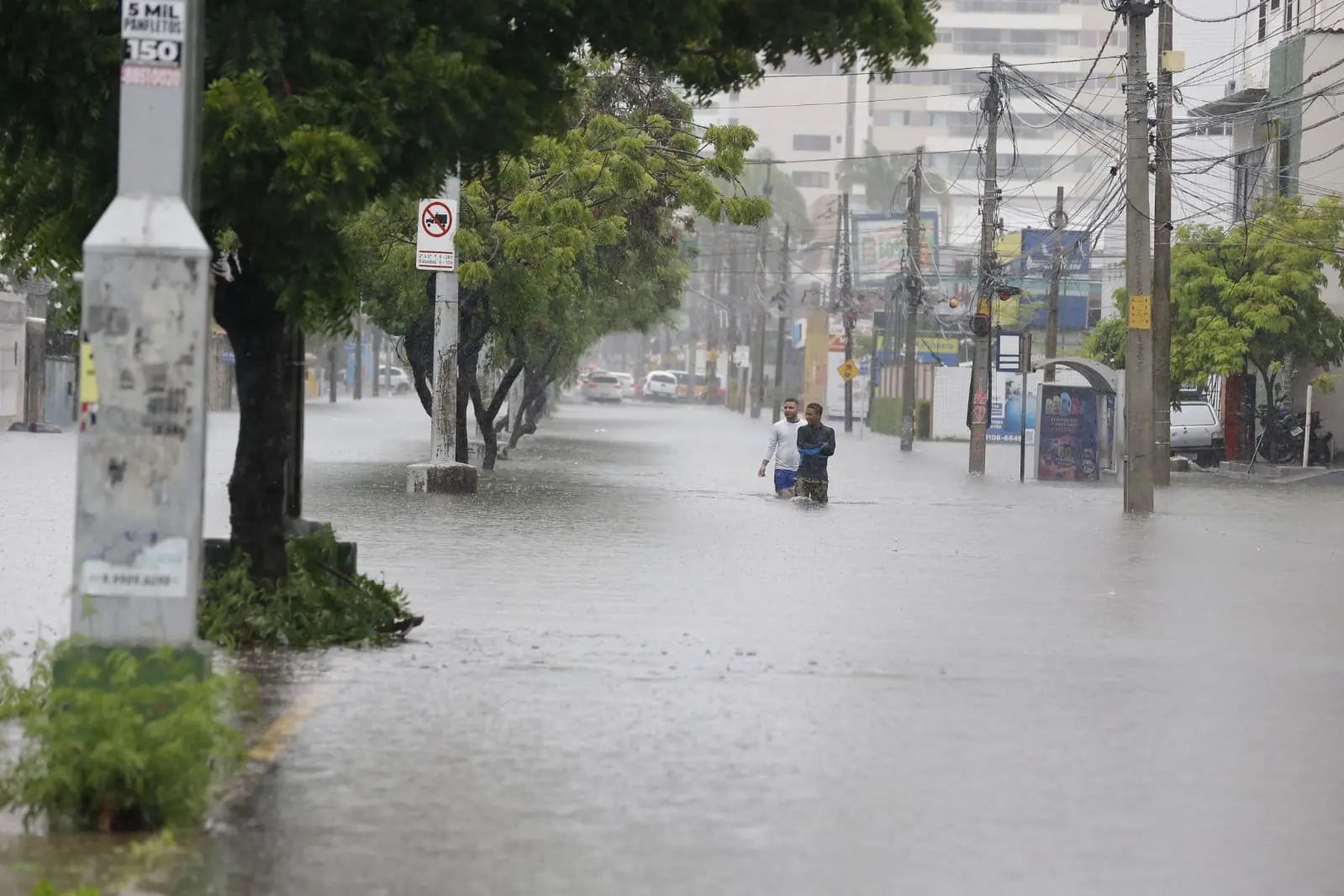 pedestres tentando atravessar avenida alagada em Fortaleza
