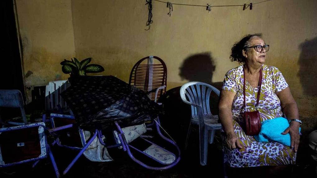 Dona Fátima usa vestido e está sentada em uma cadeira de plástico, olhando para o lado enquanto chora