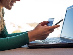 Mulher sorri enquanto segura um cartão de crédito e usa um laptop