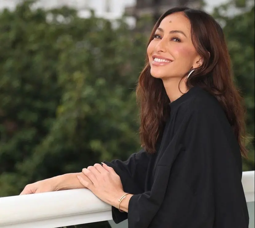 Sabrina Sato de perfil, sorrindo. Ela tem longos cabelos castanhos e um sinal na testa. Está usando brincos de argola grandes.