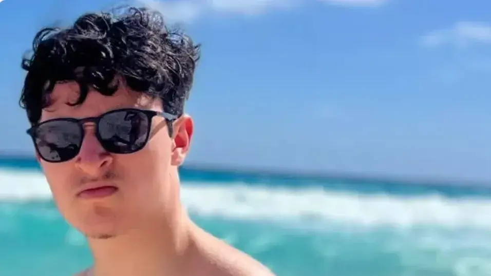 Gabriel Magalhães é branco e de cabelos pretos ondulados. Ele está na praia usando óculos escuros