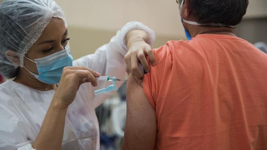 Mulher aplica dose de vacina em braço de homem