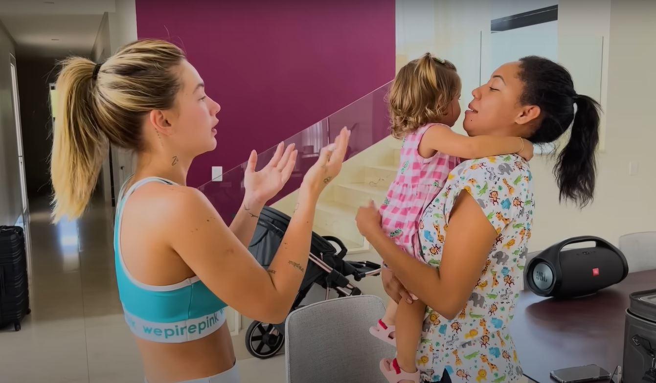 virginia estende os braços para pegar a filha do colo da babá durante vacinação