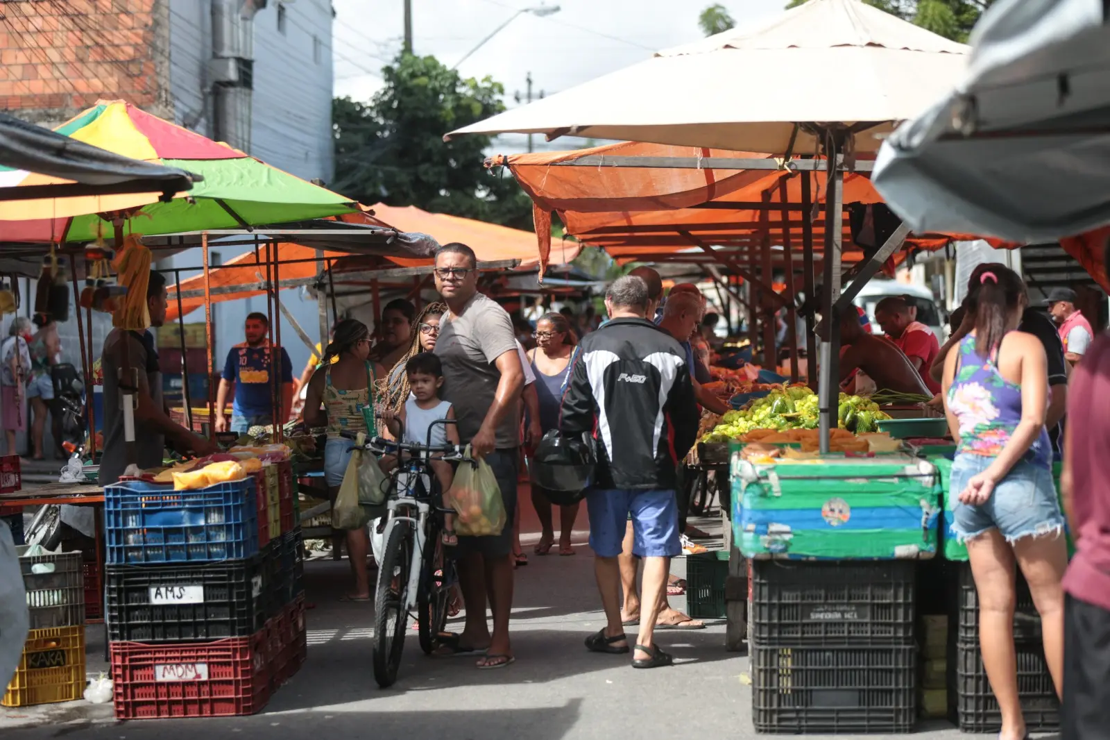 Pai com filho na bicicleta passa pela feira