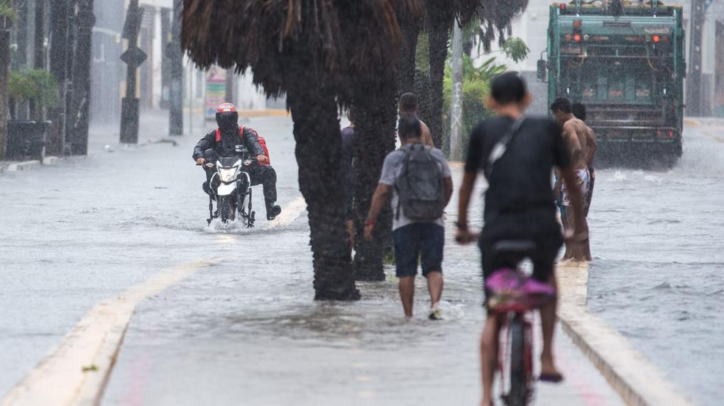 Avenida Historiador Raimundo Girão, em Fortaleza, alagada. Na foto, um motoqueiro, uma pessoa de bicicleta e pessoas a pé tentam passar pela água