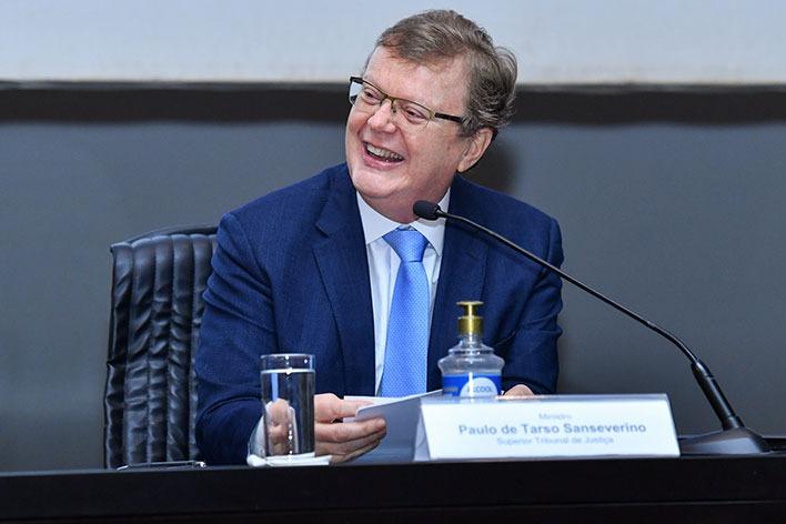 Paulo é um homem branco, de cabelos finos. Ele usa óculos e um terno azul sobre uma camisa branca com gravata azul