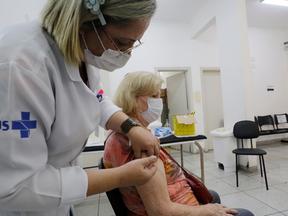 Médica aplica injeção em paciente idosa que está sentada num posto de saúde