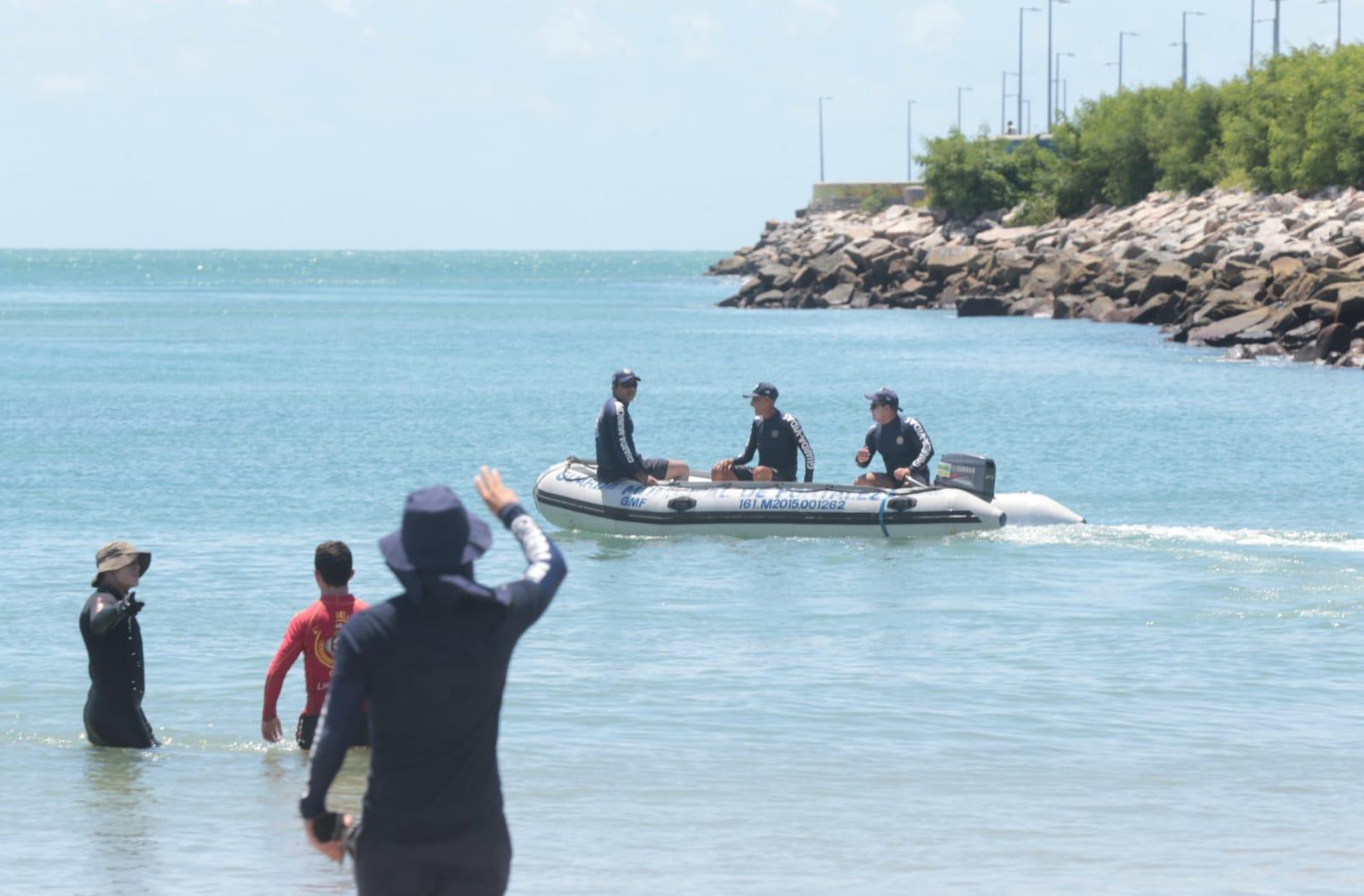 barco e bombeiros fazendo buscas no mar, ao lado de espigão