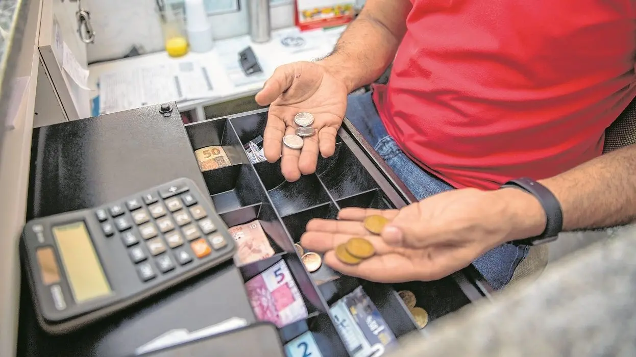 Homem segura moedas em caixa registradora
