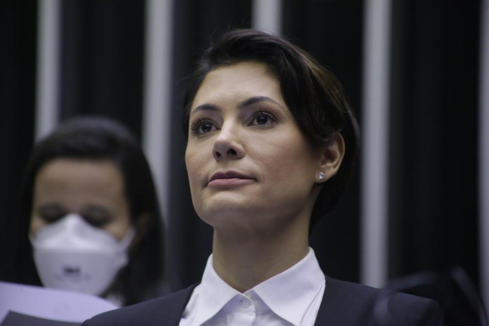 Michelle Bolsonaro é uma mulher branca, de cabelo preto e curto. Ela está séria, olhando para cima