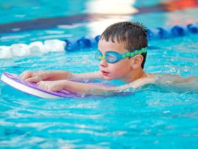 menino fazendo natação, de óculos e com prancha